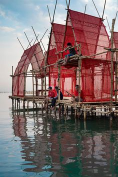 some people are sitting on a boat in the water with red netting covering it's roof