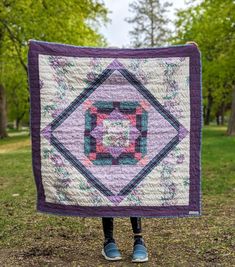 a person standing in the grass holding up a quilt