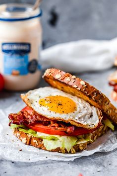 a sandwich with bacon, lettuce, tomato and an egg on it next to a jar of yogurt