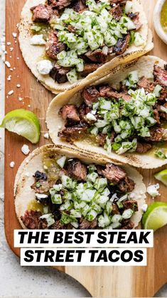 three steak tacos on a cutting board with limes and cilantro sauce