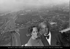 an old black and white photo of two people standing in front of a cityscape