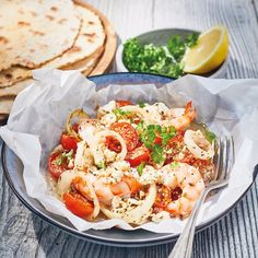 a bowl filled with pasta and shrimp on top of a table next to pita bread