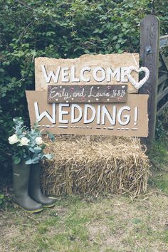 a welcome sign in front of a hay bale with flowers and boots on it