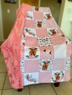 a pink and white patchwork table cloth with animals on it, sitting on a wooden chair