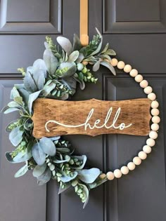 a wooden sign that says hello hanging on the front door with greenery around it