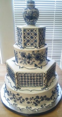 a three tiered cake with blue and white designs on the top, sitting on a table in front of a window