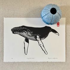 a blue vase sitting next to a black and white whale print on a piece of paper