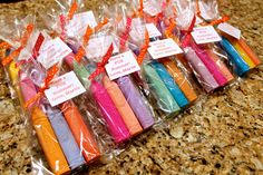 there are many different colored candles wrapped in plastic bags on the counter top with tags attached to them