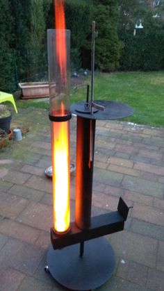 an outdoor fire pit with a glass cylinder on it's stand and flame coming out of the top