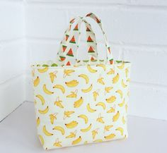 a white bag with yellow bananas and watermelon on it, sitting next to a brick wall