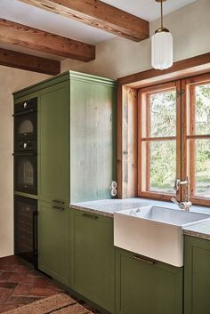 a kitchen with green cabinets and a white sink in front of a large open window