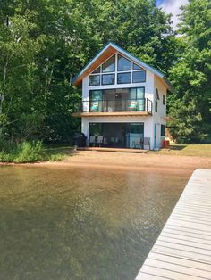 a house sitting on top of a body of water next to a wooden dock and forest