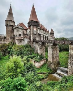 an old castle with towers and water in the foreground, surrounded by greenery