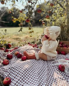 a baby doll sitting on top of a blanket next to an apple tree filled with apples