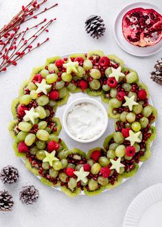 a wreath made out of grapes, raspberries and pine cones on a plate