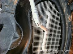 the inside of an old black trash can with a white and gray pipe sticking out of it