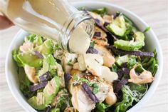 someone pouring dressing into a salad in a bowl