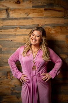 a woman standing in front of a wooden wall with her hands on her hips and smiling