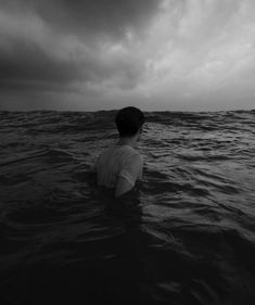 a person in the water looking out to sea under a cloudy sky with dark clouds