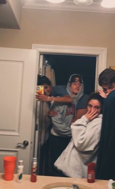 a group of people standing in front of a bathroom mirror with one person covering his face