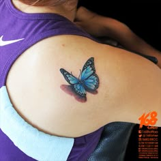 a blue butterfly tattoo on the back of a woman's left shoulder and upper arm