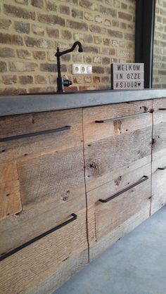 a bathroom vanity made out of wood with a brick wall behind it and a sign on the counter