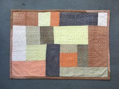 a patchwork quilt is hanging on the wall in front of a gray background with an orange, yellow and black square pattern