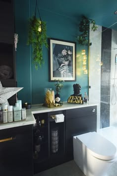 a bathroom with blue walls and black cabinets, white toilet and green plants on the wall