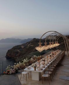 an outdoor dining area overlooking the ocean with chandeliers hanging from it's ceiling