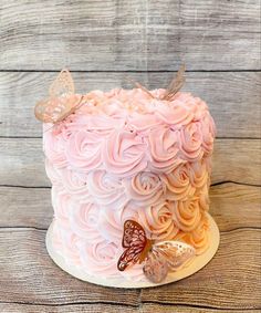 a cake with pink frosting and butterflies on top, sitting on a wooden table