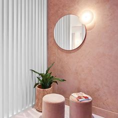 a bathroom with a round mirror on the wall next to two stools and a potted plant