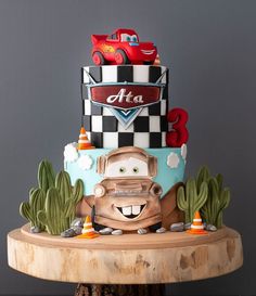 a three tiered cake with cars on top and cactus around the edges, sitting on a wooden stand