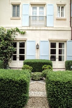 a house with blue shutters on the windows and bushes in front of it,