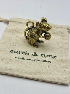 a small gold mouse brooch sitting on top of a cloth bag with the words earth & time printed on it