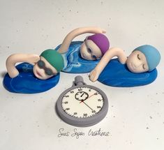 two figurines are laying on their stomachs next to a clock that reads 3 o'clock