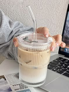 a person holding a drink in front of a laptop