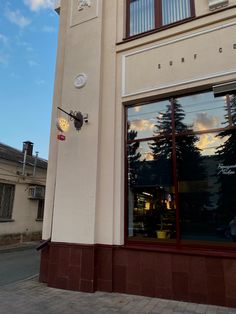 a clock on the side of a building next to a window with trees reflected in it