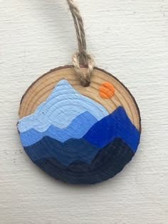 a wooden ornament hanging on a rope with mountains painted in blue and orange