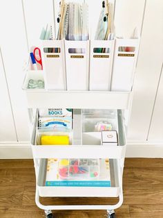 a white cart filled with lots of craft supplies on top of a hard wood floor