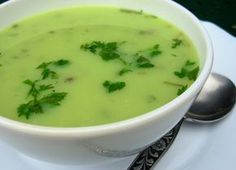 a white bowl filled with green soup on top of a plate next to a spoon