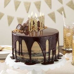 a birthday cake with chocolate icing and lit candles on top, sitting on a table