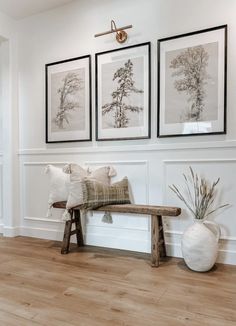 three framed pictures hang on the wall above a wooden bench in a white living room