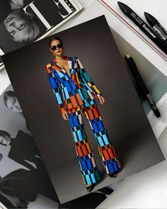 a woman in a colorful suit and sunglasses on top of a magazine next to some pens