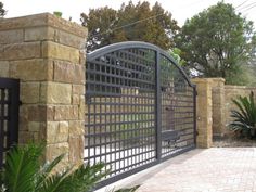 an iron gate and brick wall in front of a stone fence with plants on the side