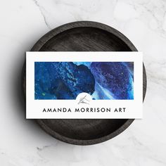 a blue and white business card with the words amanda morrison art on it in front of a wooden bowl