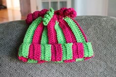 a crocheted pink and green hat sitting on top of a gray couch next to a window