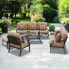 the patio furniture is set up outside in the yard with flowers and trees behind it