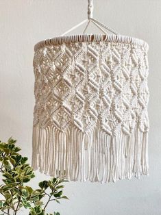 a white macrame hanging from a hook on a wall next to a potted plant