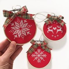 three red ornaments with white snowflakes are being held by someone's hand