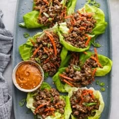 lettuce wraps with ground beef and carrots on a blue plate next to dipping sauce